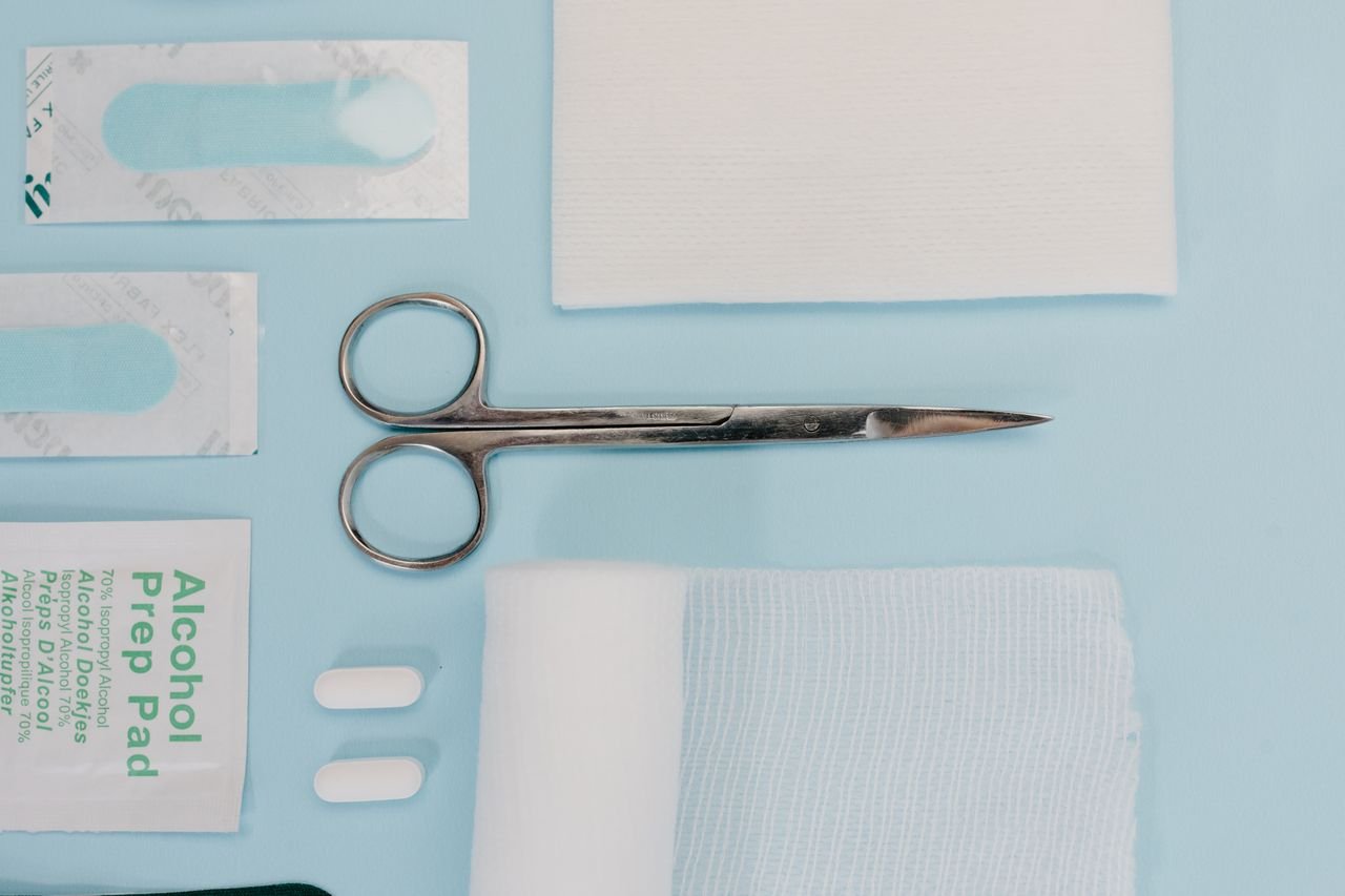 Top view of various medical supplies including scissors, bandages, and prep pads on a blue surface.